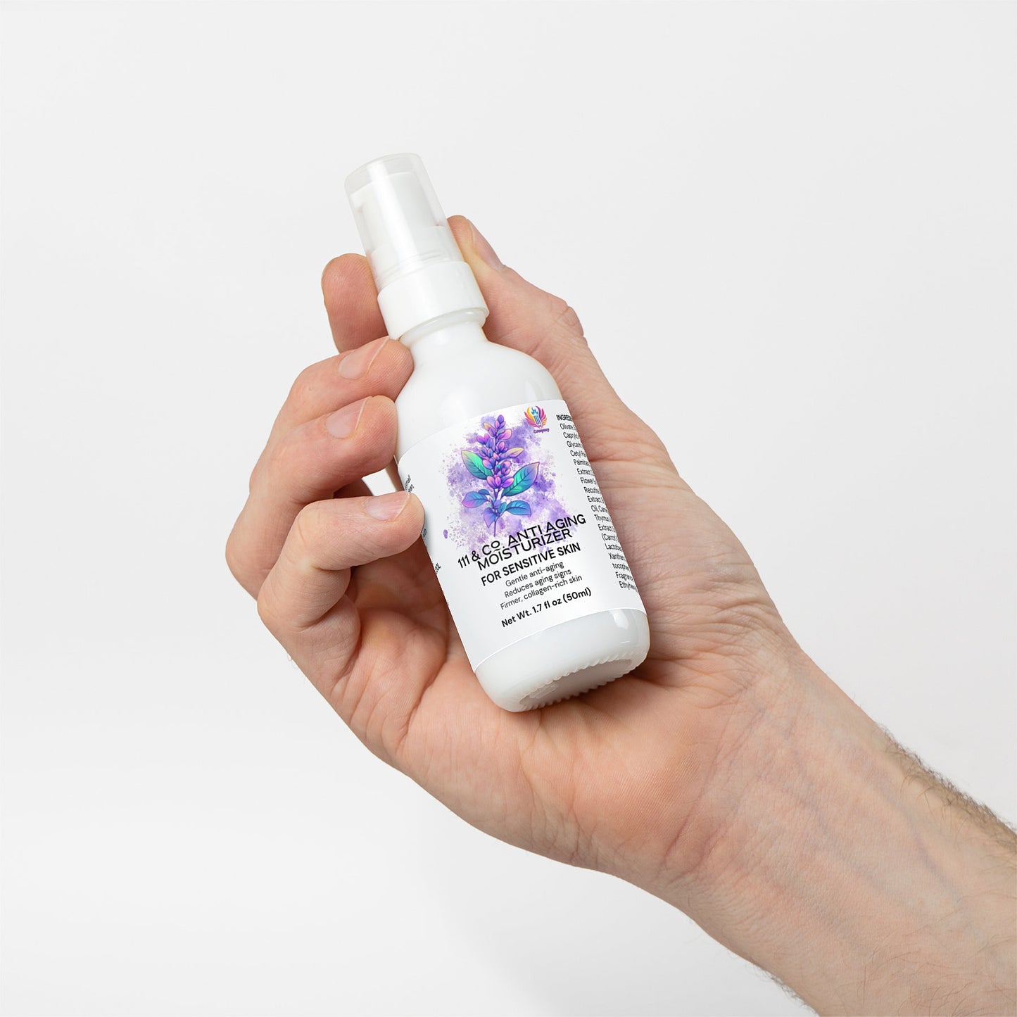 A hand holds a white spray bottle of 111 & Co. Anti-Aging Moisturizer for sensitive skin, enriched to boost collagen production. Adorned with purple flowers and product details, the label suggests it enhances skin elasticity. The backdrop is a simple white.