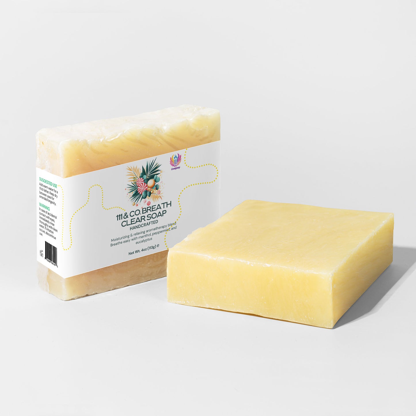 A light yellow moisturizing soap bar sits beside its partially transparent rectangular packaging. The label says 111 & Company Breathe Clear Soap, featuring tea tree leaves and colorful flowers, with a white background and green text details.