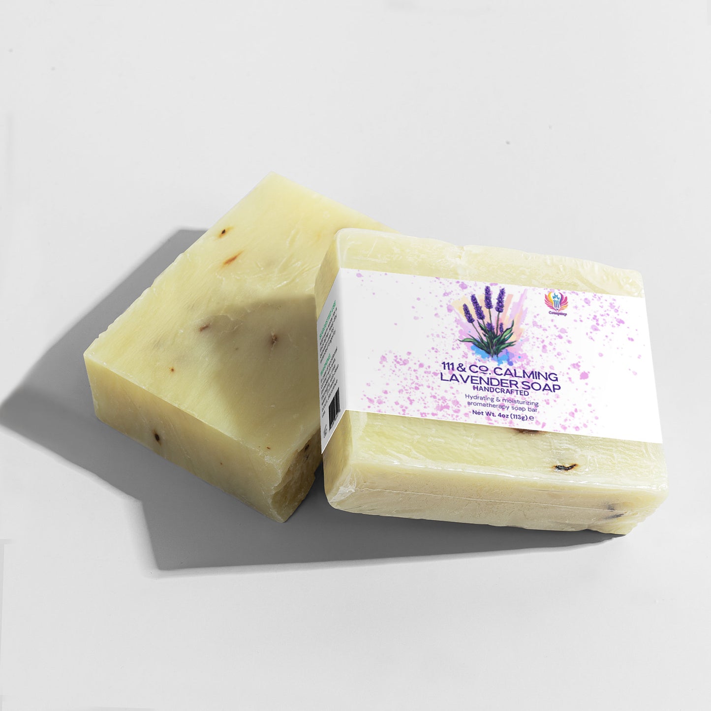 Two rectangular bars of 111 & COMPANY CALMING LAVENDER SOAP sit on a light gray surface. With a pale yellow hue and speckled texture, they complement the labels lavender design. Perfect for sensitive skin, the unwrapped bar reveals a smooth texture casting leftward shadows.