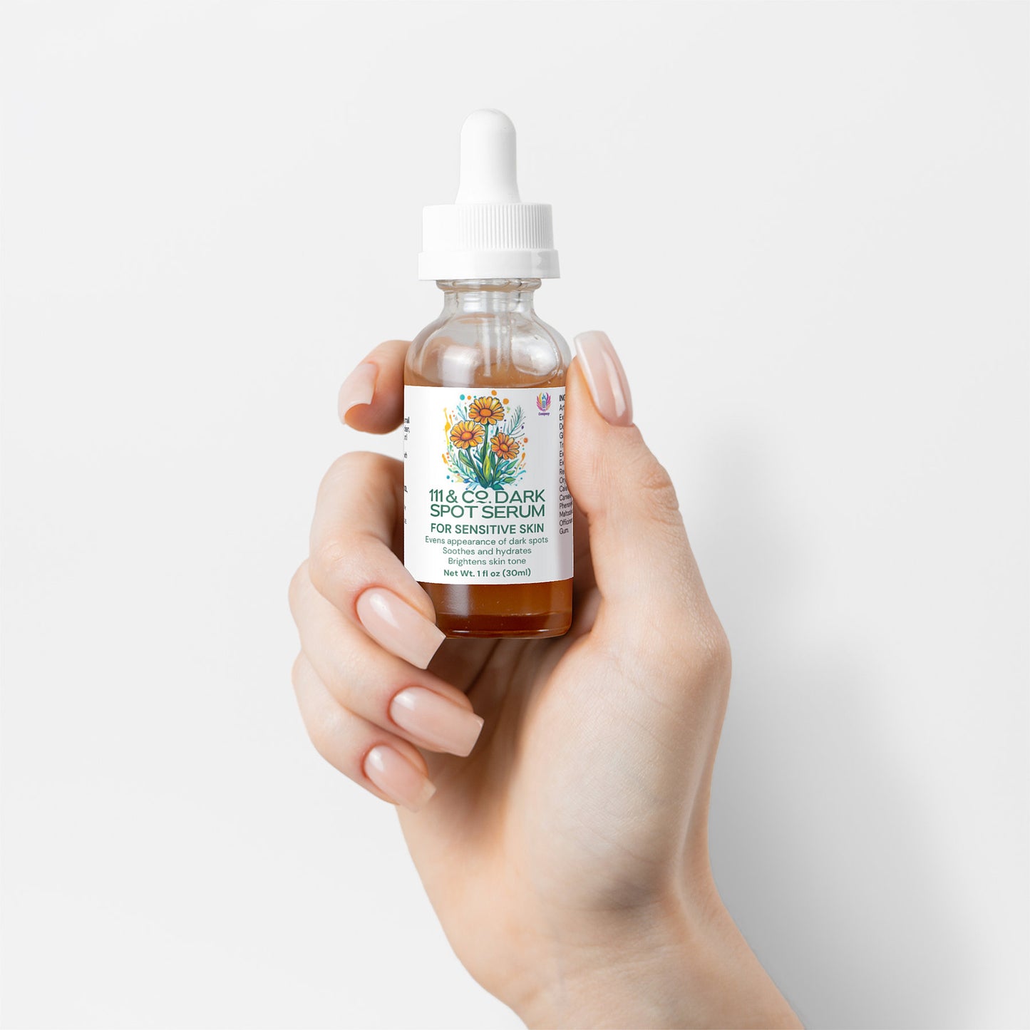 A hand with manicured nails holds a clear bottle with a white dropper cap. The label reads, 111 & COMPANY DARK SPOT SERUM FOR SENSITIVE SKIN, showcasing natural ingredients. The amber serum stands out against the plain white backdrop, adorned with vibrant floral artwork.