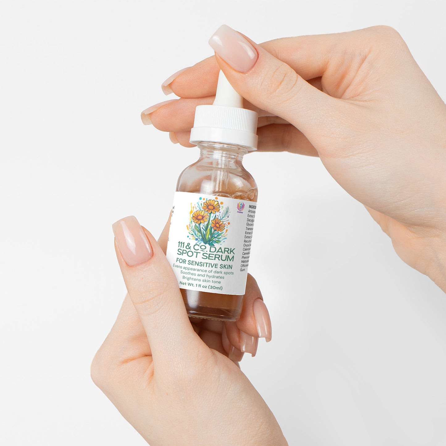 A close-up shows manicured hands holding a glass bottle of 111 & Company Dark Spot Serum for Sensitive Skin. The dropper cap and colorful floral label accentuate its natural ingredients, with For Sensitive Skin prominently displayed. A plain white backdrop highlights its purity.