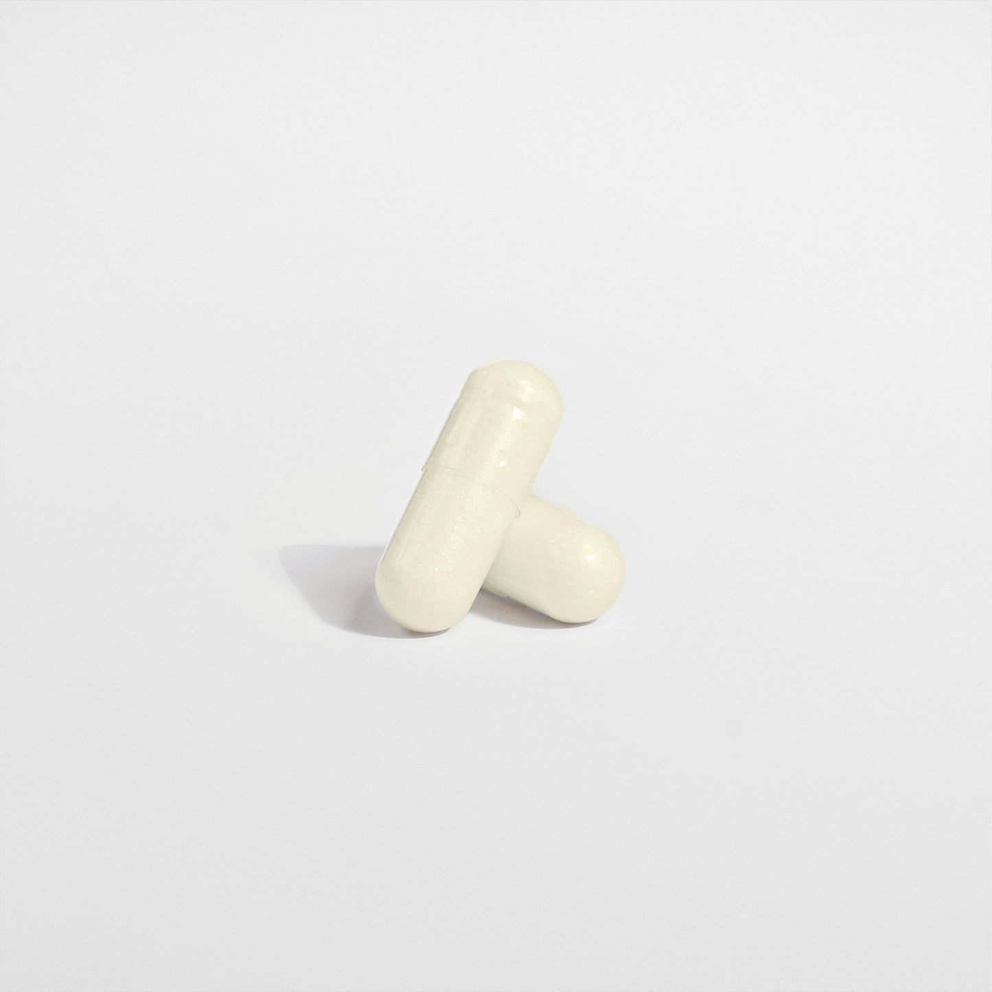 The minimalist image shows two white capsules of 111 & COMPANY DIGESTIVE ENZYME PRO BLEND by 111 & Company on a plain background. One leans diagonally against the other, both casting soft shadows, highlighting their smooth textures and seam lines for a simple, clean look.