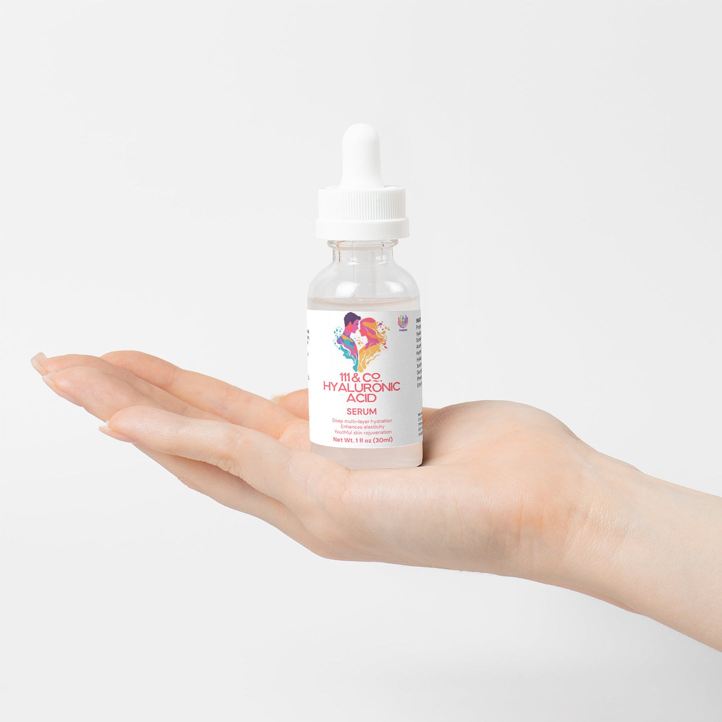 A hand holds a small clear bottle of serum with a dropper cap. The label reads 111 & Company Hyaluronic Acid Serum and features colorful abstract designs. This rejuvenating, hydrating serum stands out against the plain white background, highlighting the product and the light skin tone of the hand.
