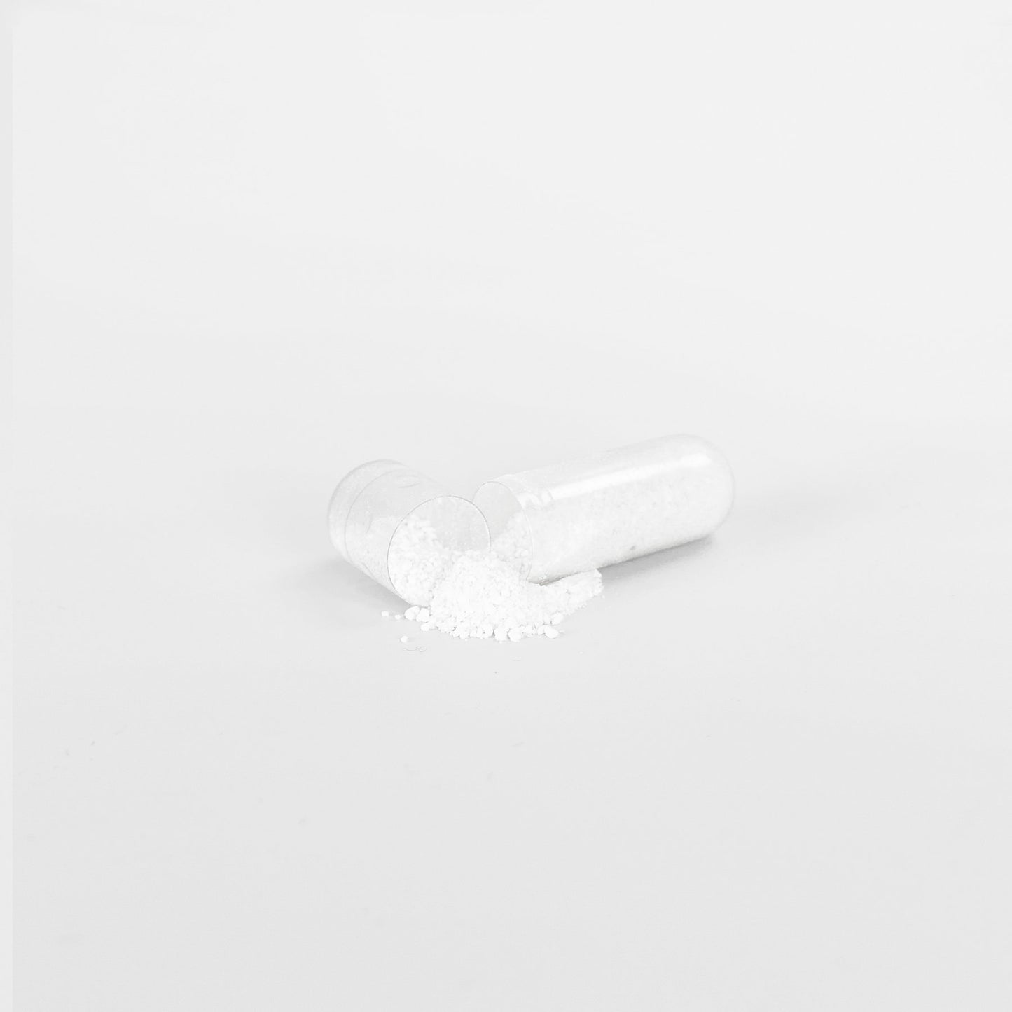 A clear capsule of 111 & COMPANY KETO BHB lies split open on a white background, its fine powder spilled out. This minimalist scene captures the clinical essence of 111 & Company keto aid designed for supporting ketosis transition.