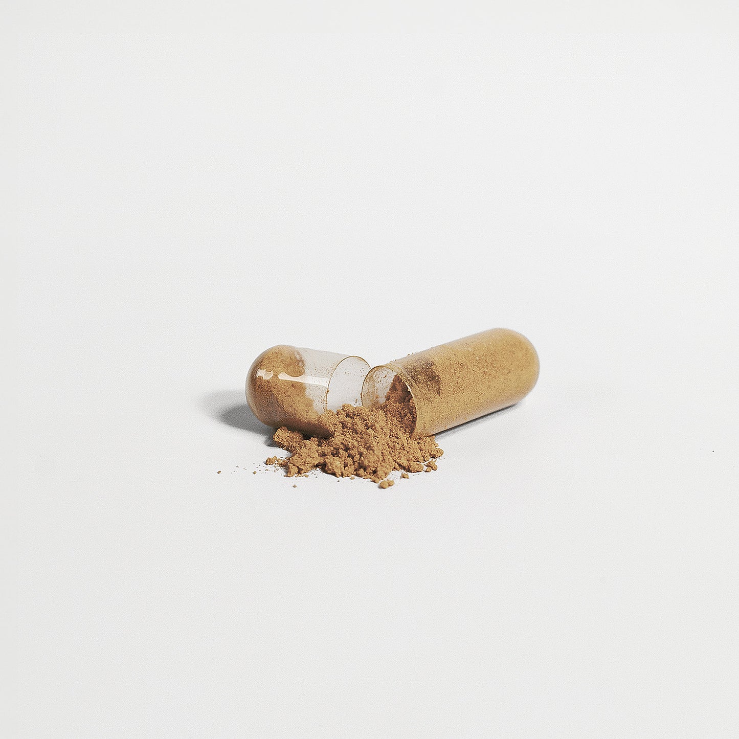 A transparent capsule of 111 & COMPANY LIVER SUPPORT CAPSULES by 111 & Company lies on a white backdrop, spilling light brown detox powder. The emptier half is on the left, creating a small mound next to the intact right half.