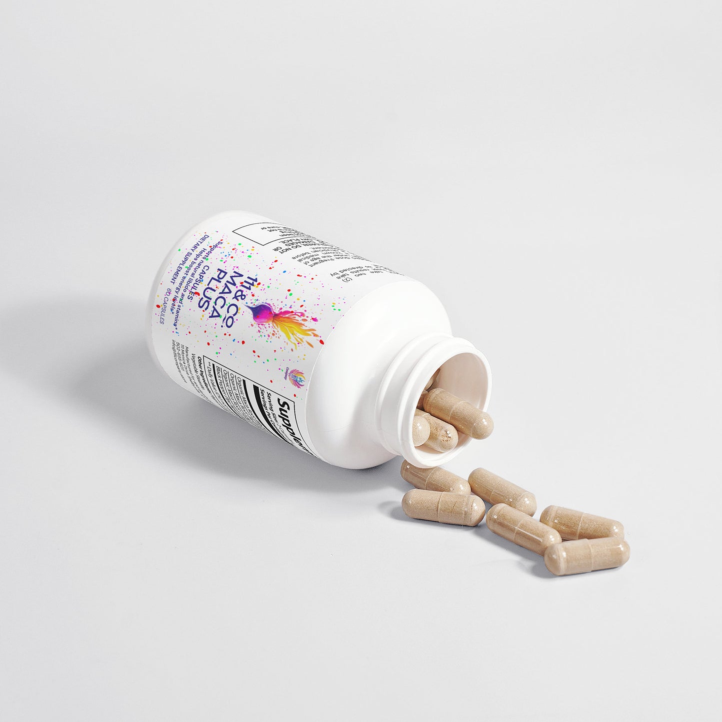 A white 111 & COMPANY MACA PLUS CAPSULES bottle by 111 & Company lies on its side, with tan capsules spilling onto a white surface. The colorful abstract design promotes energy enhancement, while the visible text details ingredients and instructions for this Maca supplement.