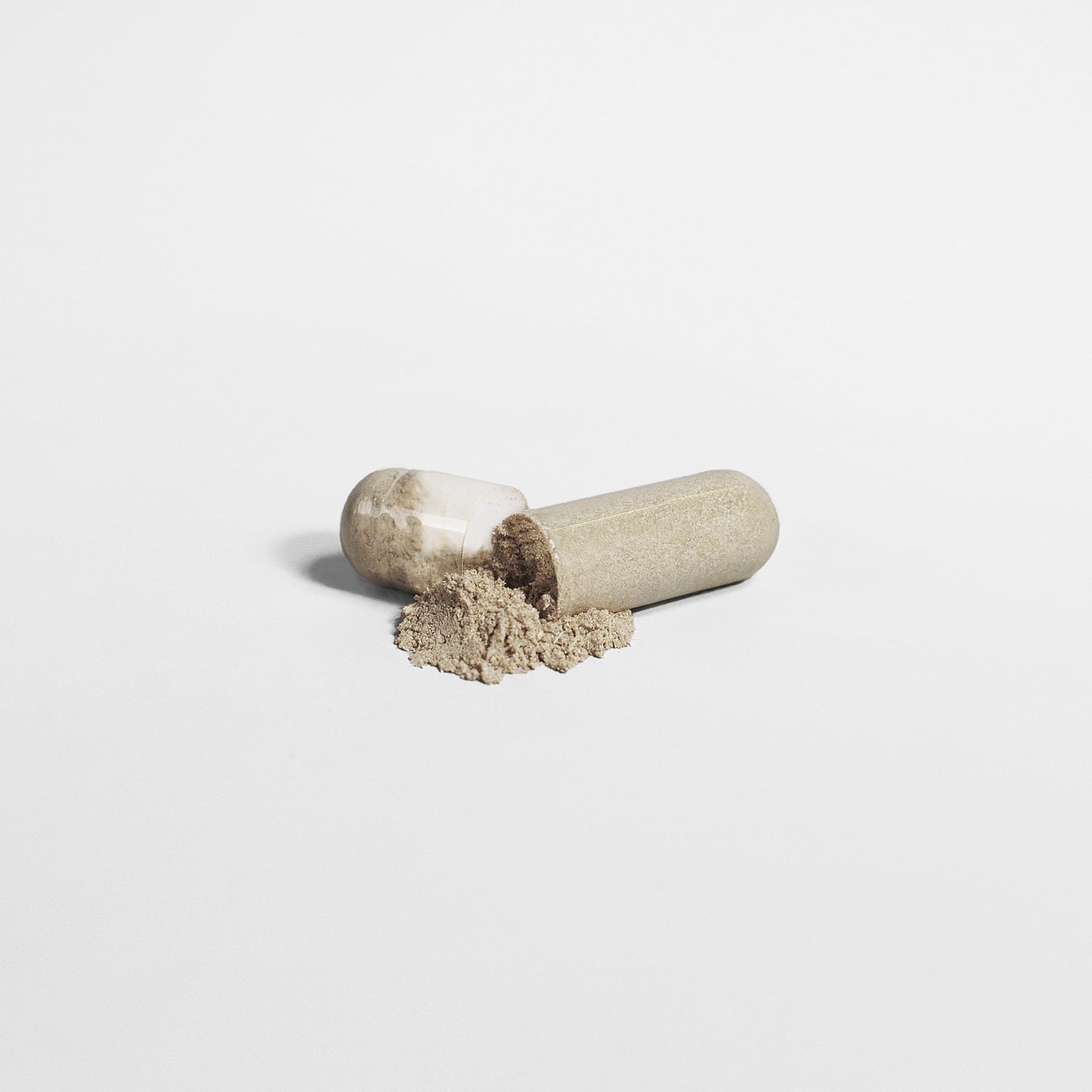 A clear capsule, likely a 111 & Company Max Detox (Acai Detox), has split open, spilling beige powder onto a white surface. Both halves lie horizontally, highlighting the natural texture and color of the contents.