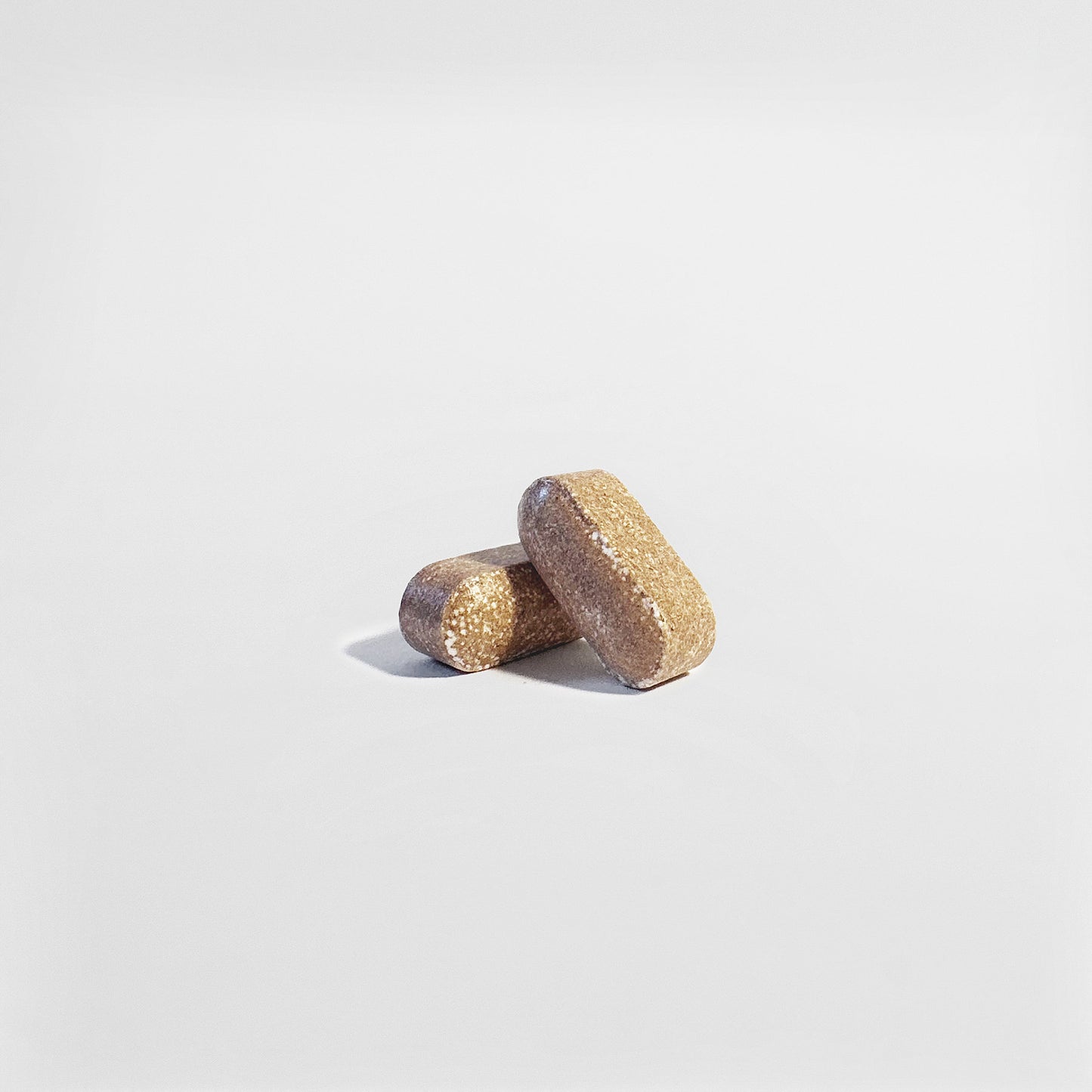 Two rectangular, brown 111 & COMPANY MENS VITALITY TABLETS by 111 & Company rest on a smooth white background. These dietary supplements reflect light slightly, emphasizing their coarse texture and granular surfaces.