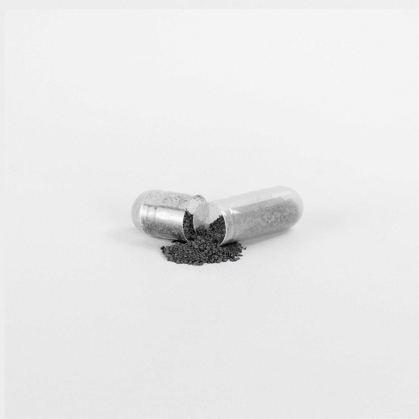 A 111 & COMPANY NATURAL GUT WELLNESS CAPSULE from 111 & Company sits open on a white surface, fine grey powder spilling out to promote digestive wellness. Capsule halves reveal granulated fulvic acid with minimalist focus on the capsule contents.