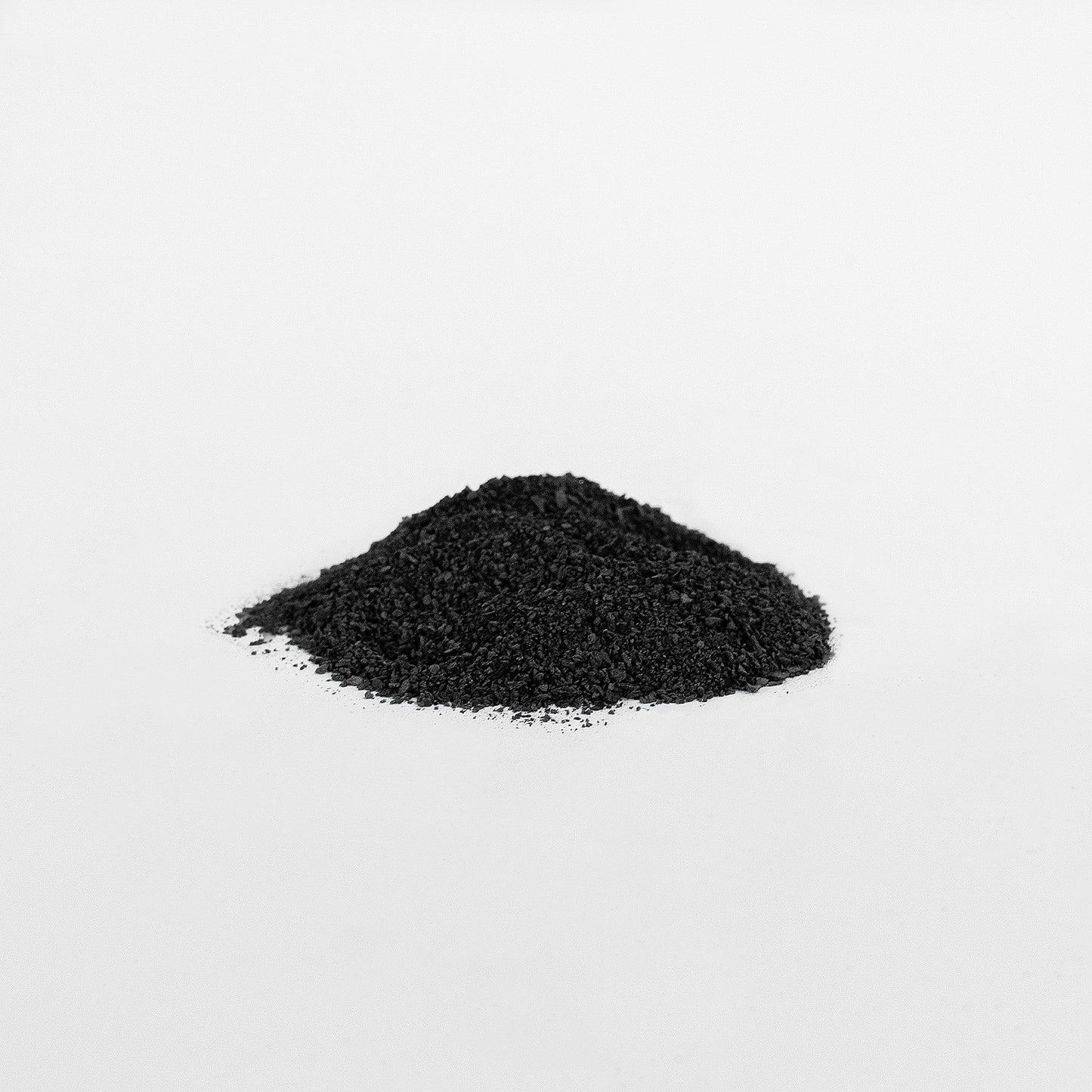 A small mound of 111 & COMPANY GUT WELLNESS POWDER by 111 & Company, enriched with fulvic acid, sits on a smooth white surface. The fine black powders granular texture highlights its potential digestive benefits against the plain background.