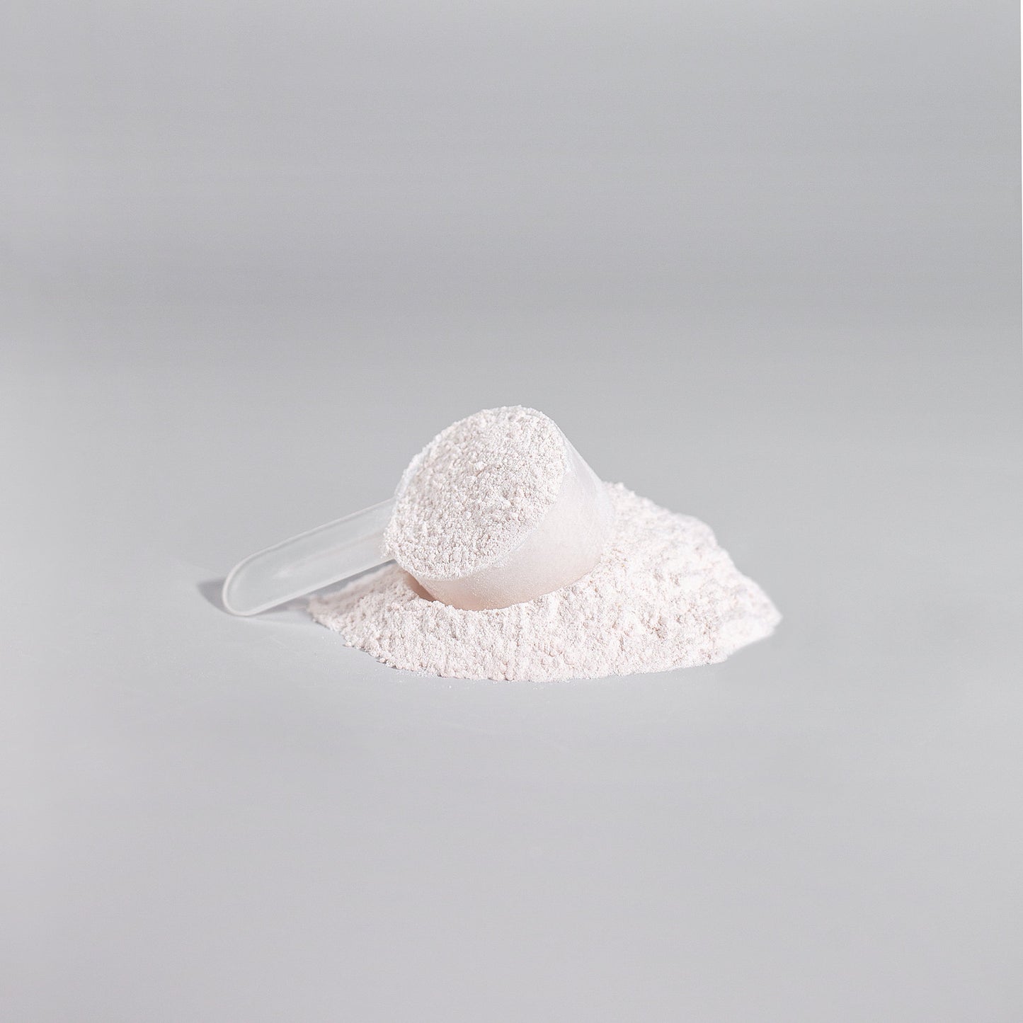 A clear plastic scoop filled with 111 & COMPANY NITRIC SHOCK PRE-WORKOUT POWDER (FRUIT PUNCH) sits on a flat gray surface, surrounded by some spilled powder forming a small mound. The smooth, light gray background enhances the scenes minimalist feel.