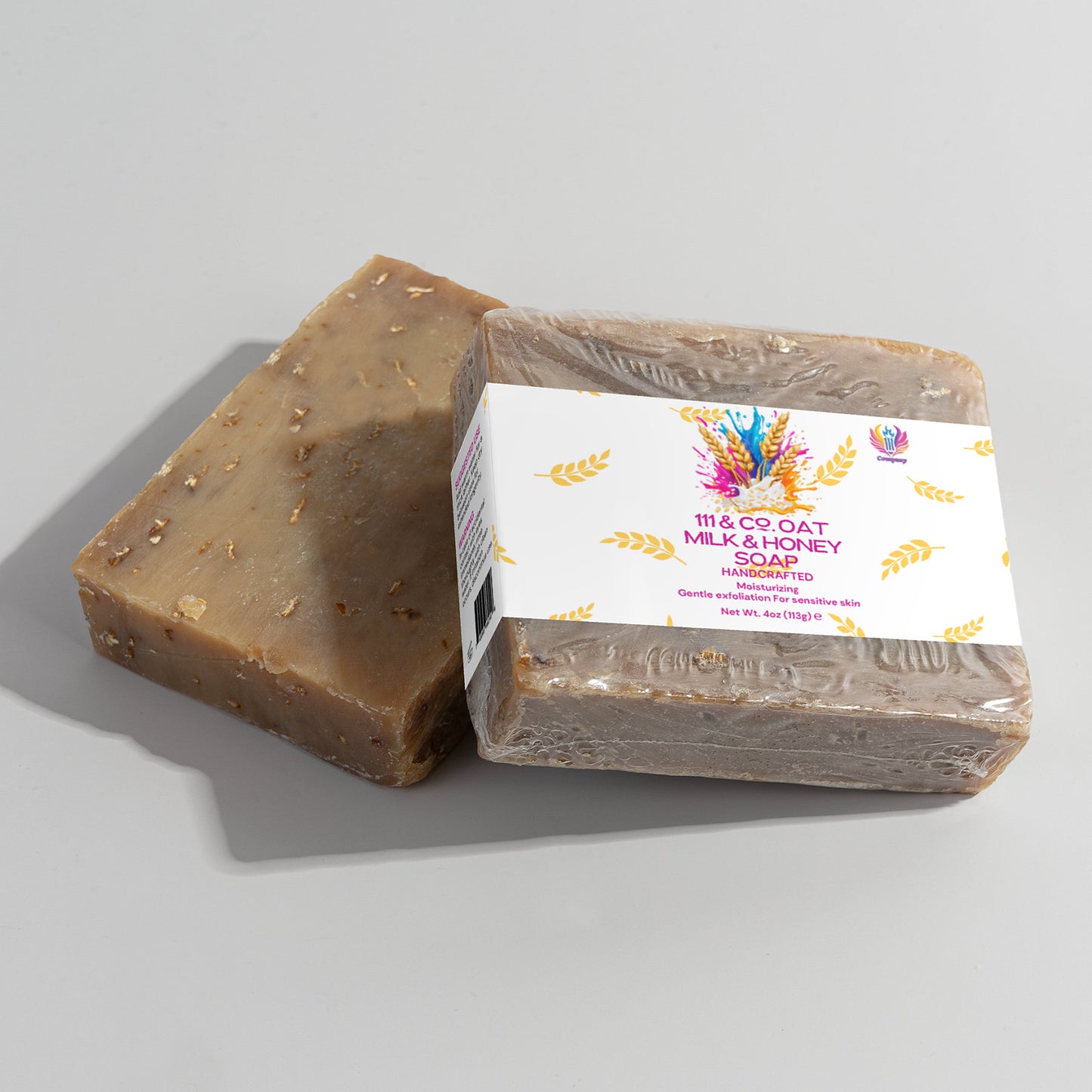 Two soap bars are shown; one is unwrapped, displaying a textured brown surface with small spots. The other is partially wrapped in clear plastic, labeled 111 & COMPANY OAT MILK HONEY SOAP, ideal for sensitive skin with its nourishing formula and colorful graphics.