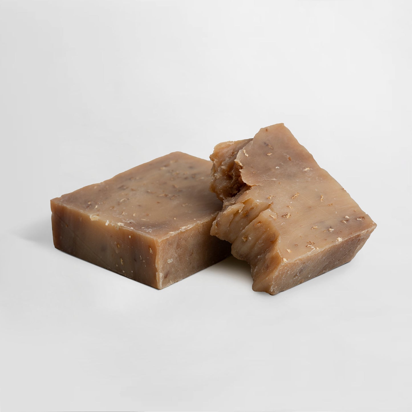 Two bars of 111 & COMPANY OAT MILK HONEY SOAP by 111 & Company sit on a white surface. One has a rugged corner, highlighting its natural look and nourishing formula. Both display small specks, perfect for sensitive skin with exfoliating benefits.