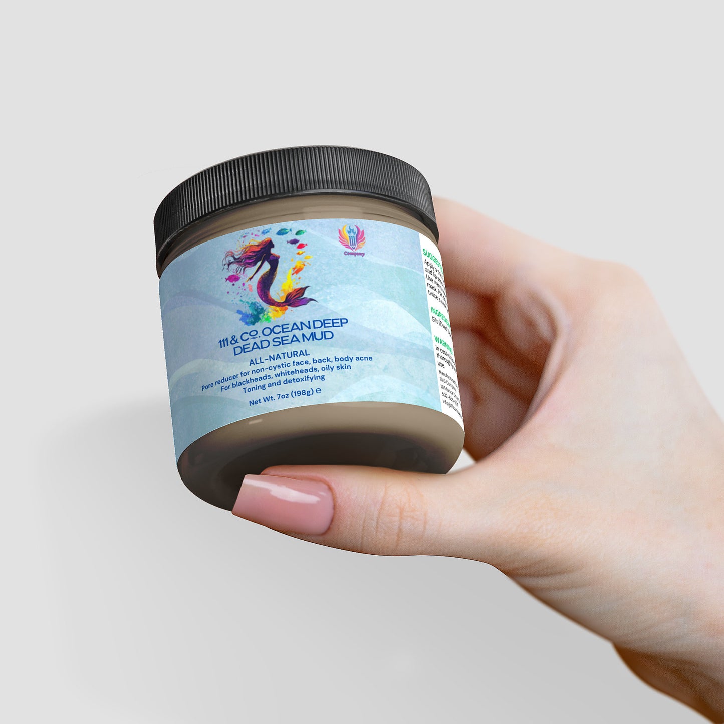 A hand holds a jar of 111 & Company Ocean Deep Dead Sea Mud from 111& Company, highlighting its mineral-rich, all-natural skincare benefits for detoxifying and rejuvenating face, hair, and body. The jar features a black lid and a colorful label with a stylized mermaid amid waves.