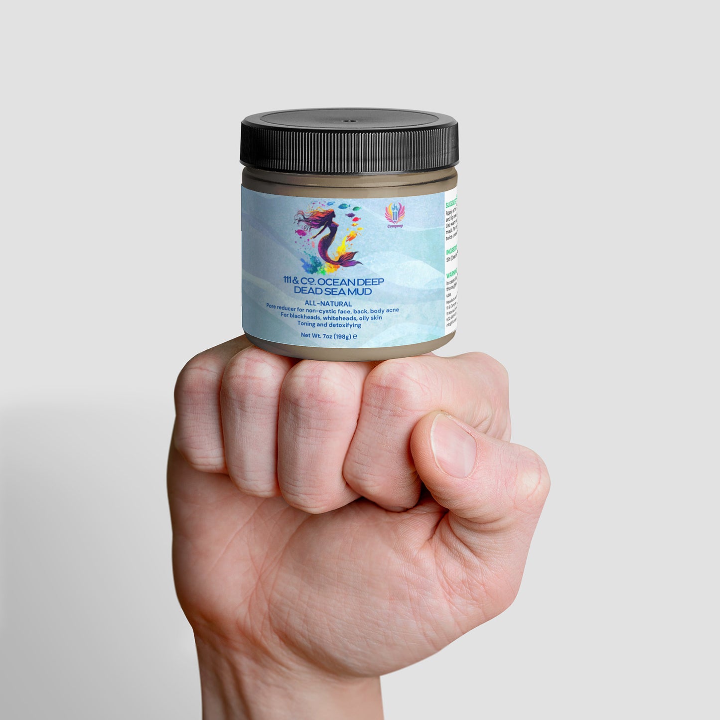 A hand holds a jar of 111 & Co. OCEAN DEEP DEAD SEA MUD by 111 & Company with a black lid. The label, featuring a colorful seahorse, boasts its all-natural, mineral-rich formula for face, body, and hair against a plain white background highlighting natural skincare benefits.