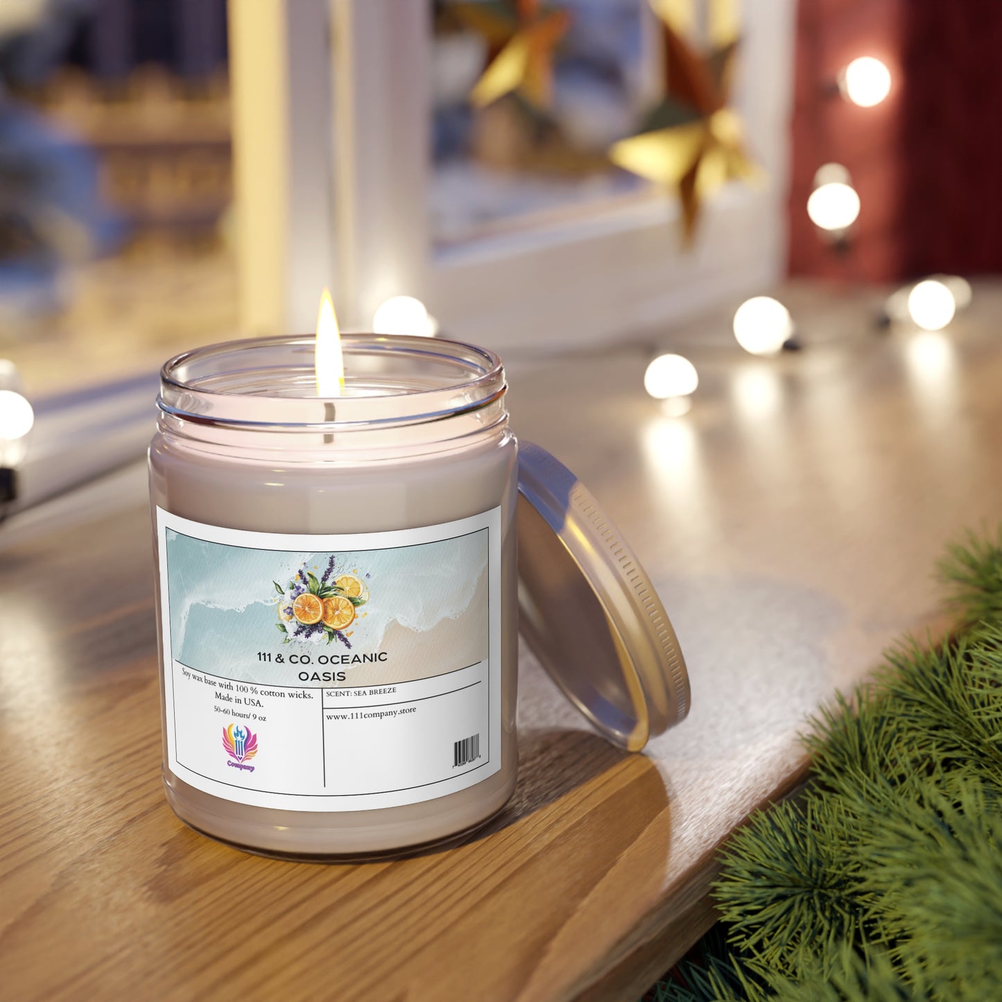 A 111 & Company Oceanic Oasis Sea Breeze Scented Candle by 111 & Company rests on wood, infused with citrus notes. Nearby greenery and a blurred backdrop of festive lights complete the scene. Its lid leans beside the candle, enhancing the cozy atmosphere.