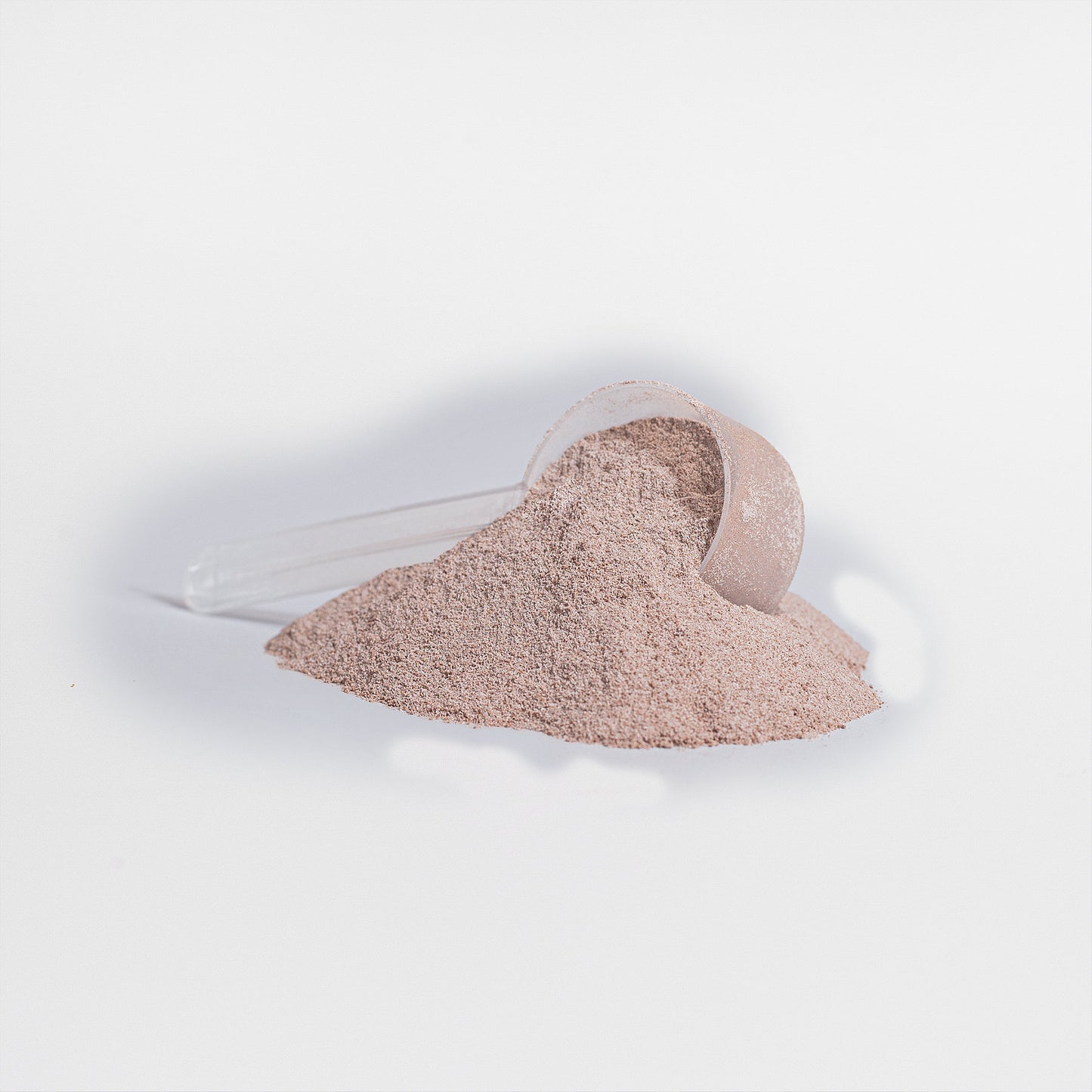 A clear scoop with a heap of fine, light brown 111 & COMPANY PLANT PROTEIN (VANILLA) by 111 & Company spills onto a smooth white surface, tilted slightly and casting a shadow. Rich in amino acids for muscle recovery, this simple scene embodies health and wellness.