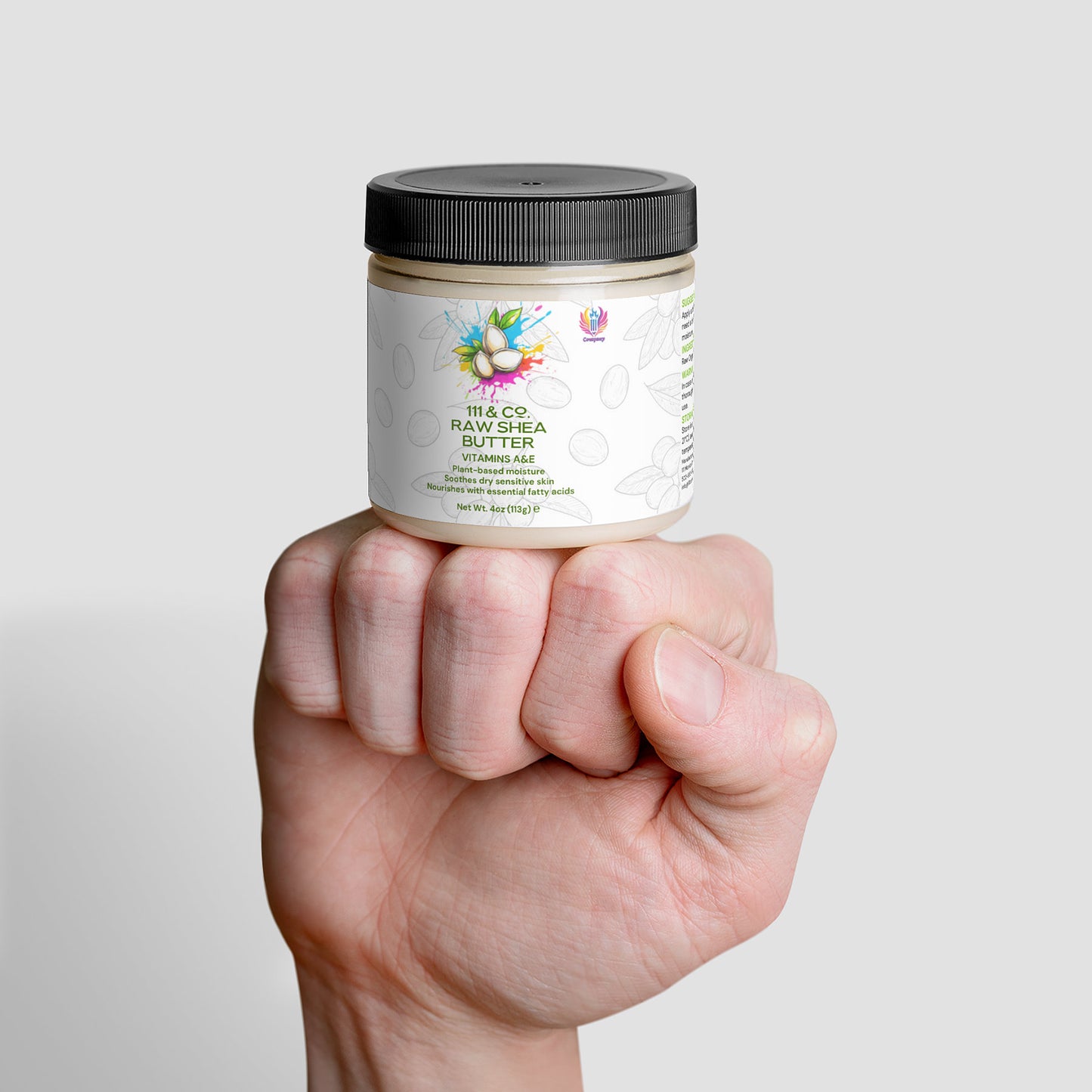 A hand holds a jar of 111 & COMPANY RAW SHEA BUTTER, a plant-based moisturizer from 111 & Company. The jar has a black lid and a label with colorful graphics stating 100% Organic Raw Shea Butter, set against a plain white background, showcasing the product prominently.