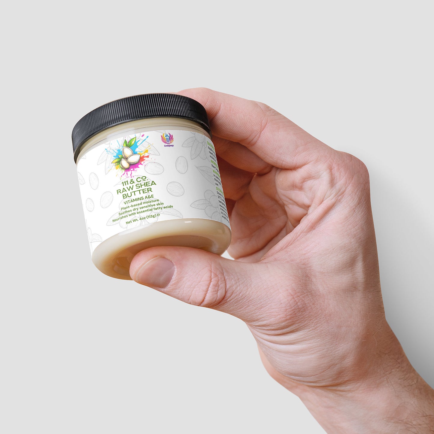 A hand holds a jar of 111 & Company Raw Shea Butter, a 114.9g plant-based moisturizer. The label shows fruit and nuts with green leaves, highlighting nourishing aloe. It has a black lid and sits against a white backdrop with subtle shadowing.