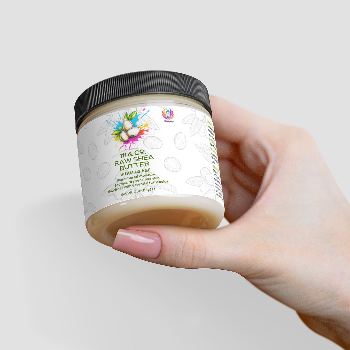 A hand displays a jar of 111 & COMPANY RAW SHEA BUTTER, a plant-based moisturizer. The black-lidded jar has a white label with an avocado illustration and colorful splashes, featuring Raw Shea Butter and vitamins A, E on a light gray background.