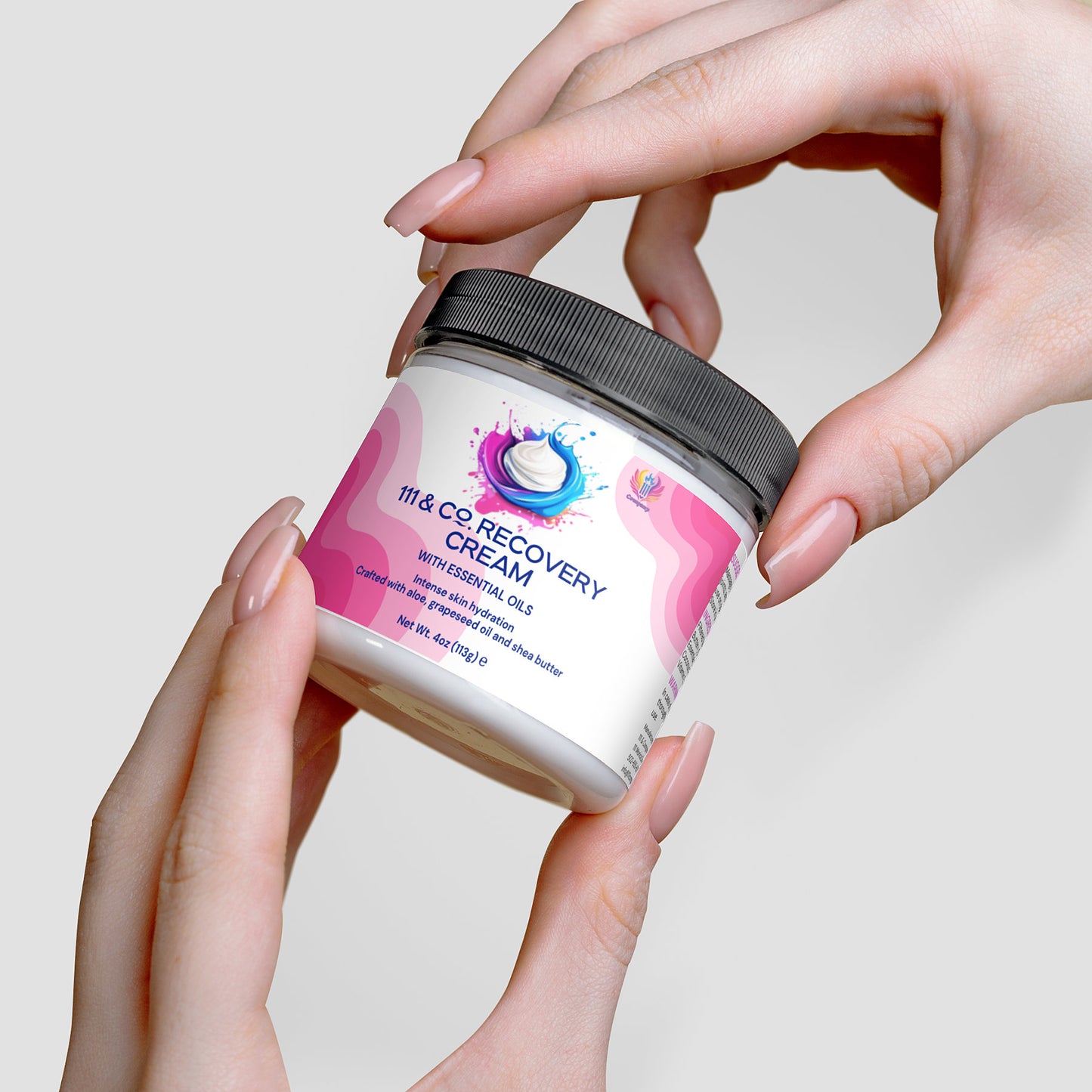 A persons hands hold a jar of 111 & Company Recovery Cream by 111 & Company, promising exceptional skin hydration. The jar features a pink and white label with a blue droplet design resembling an aloe cream, while the black lid contrasts with their neatly manicured nails.