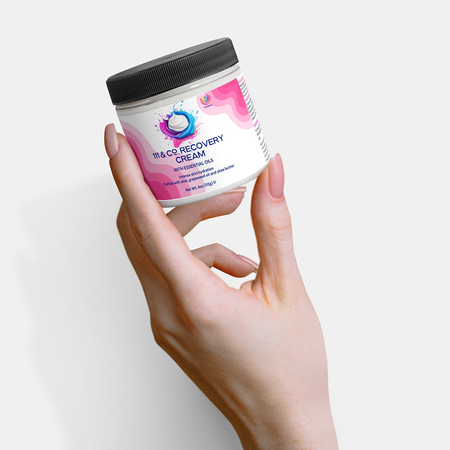 A light-skinned hand holds a 2 oz, 60 ml jar of 111 & COMPANY RECOVERY CREAM by 111 & Company. The cream features Shea Butter and Avocado for hydration. The white label has pink swirls, blue dots, and blue text. A black lid caps the jar against a pure white background.