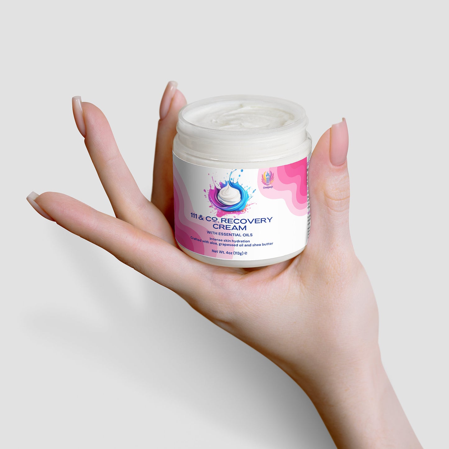 A hand gently holds a jar of 111 & COMPANY RECOVERY CREAM by 111 & Company against a light gray background. The jar, with a white lid, is adorned with vibrant blue, pink, and purple designs. The smooth white cream promises hydration. The persons nails are polished soft pink.
