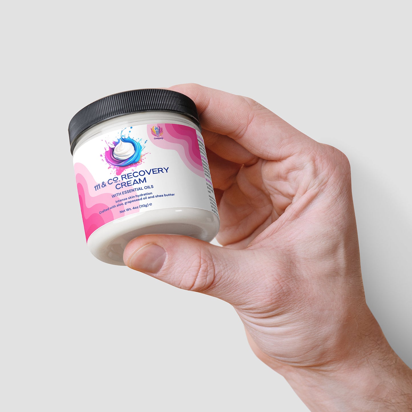 A hand holds a jar of 111 & Company Recovery Cream against a plain background. This Aloe-infused cream from 111 & Company offers natural oils for optimal skin hydration, focusing on joints and muscles. The jar features a pink and purple design with a stylized droplet logo.