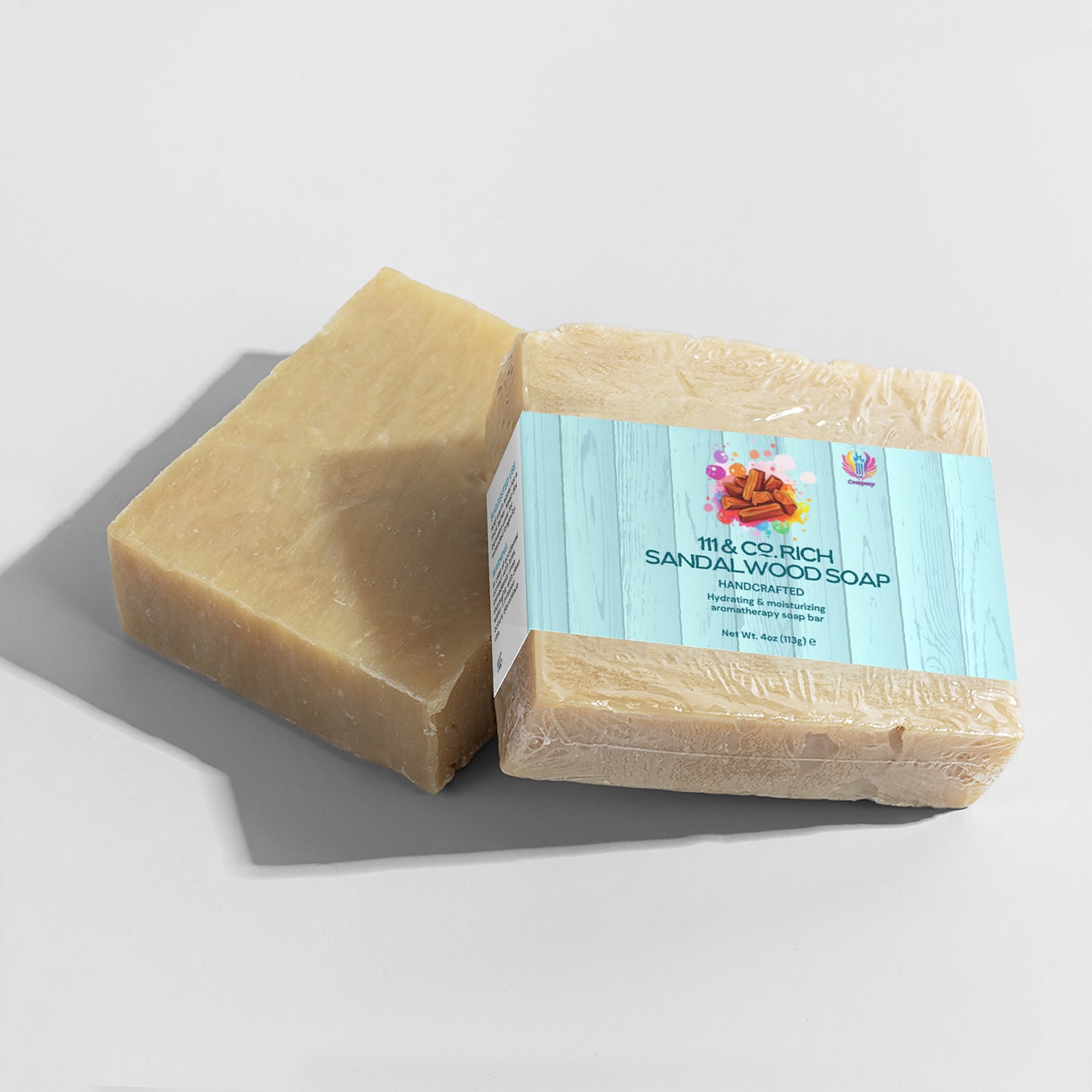 Two bars of the sand-colored, handcrafted 111 & COMPANY RICH SANDALWOOD SOAP by 111 & Company are shown. One is unwrapped, and one wrapped in plastic with a blue label featuring orange flowers and the text Moisturizing and Nourishing Rich Sandalwood Soap. Ideal for sensitive skin.