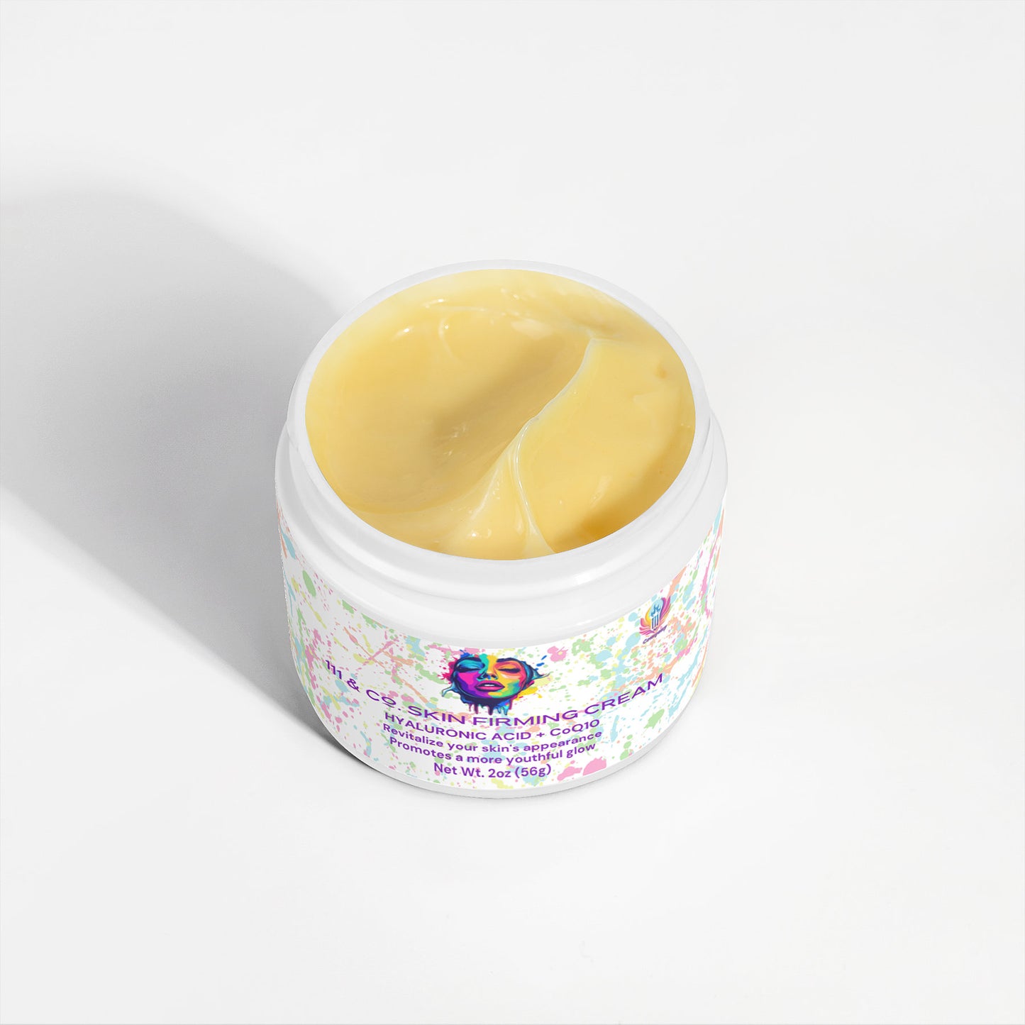 Open jar of 111 & COMPANY SKIN FIRMING CREAM by 111 & Company, featuring a colorful abstract design. This rich cream with a light yellow hue is infused with hyaluronic acid, CoQ10, and DMAE, showcasing its luxurious texture against a pristine white background.