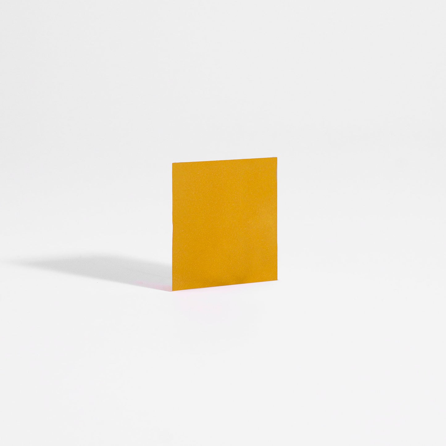 A yellow square paper stands on a smooth white surface, evoking tranquility like the calming effect of 111 & COMPANY SLEEP STRIPS BAG. A right-side light source casts a soft shadow, enhanced by the serene seamless white backdrop.
