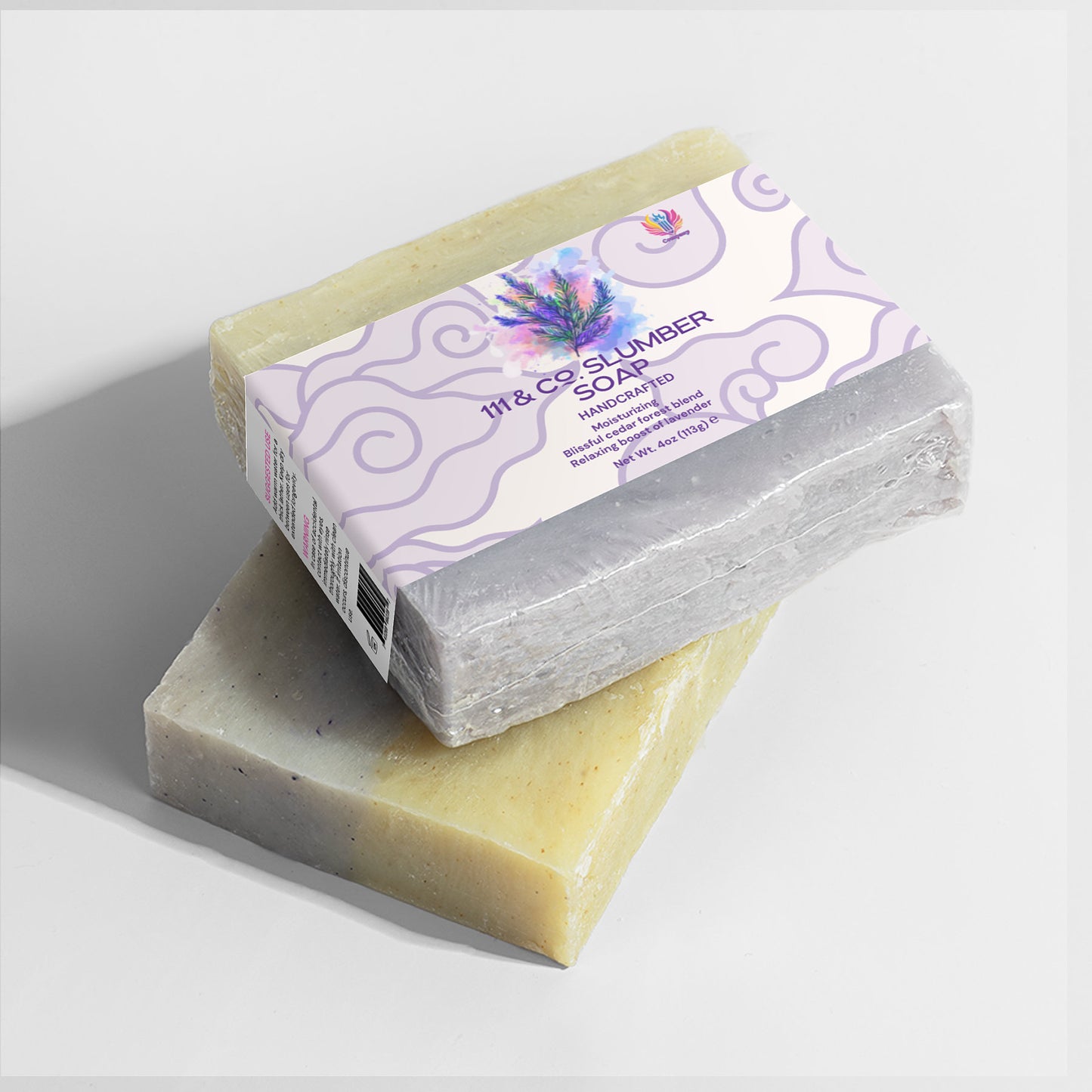Two handcrafted soap bars are on a white surface. The top bar, wrapped in purple floral packaging, is labeled 111 & COMPANY SLUMBER SOAP from 111 & Company and has a lavender scent. The bottom bar is unwrapped, speckled, and rectangular.