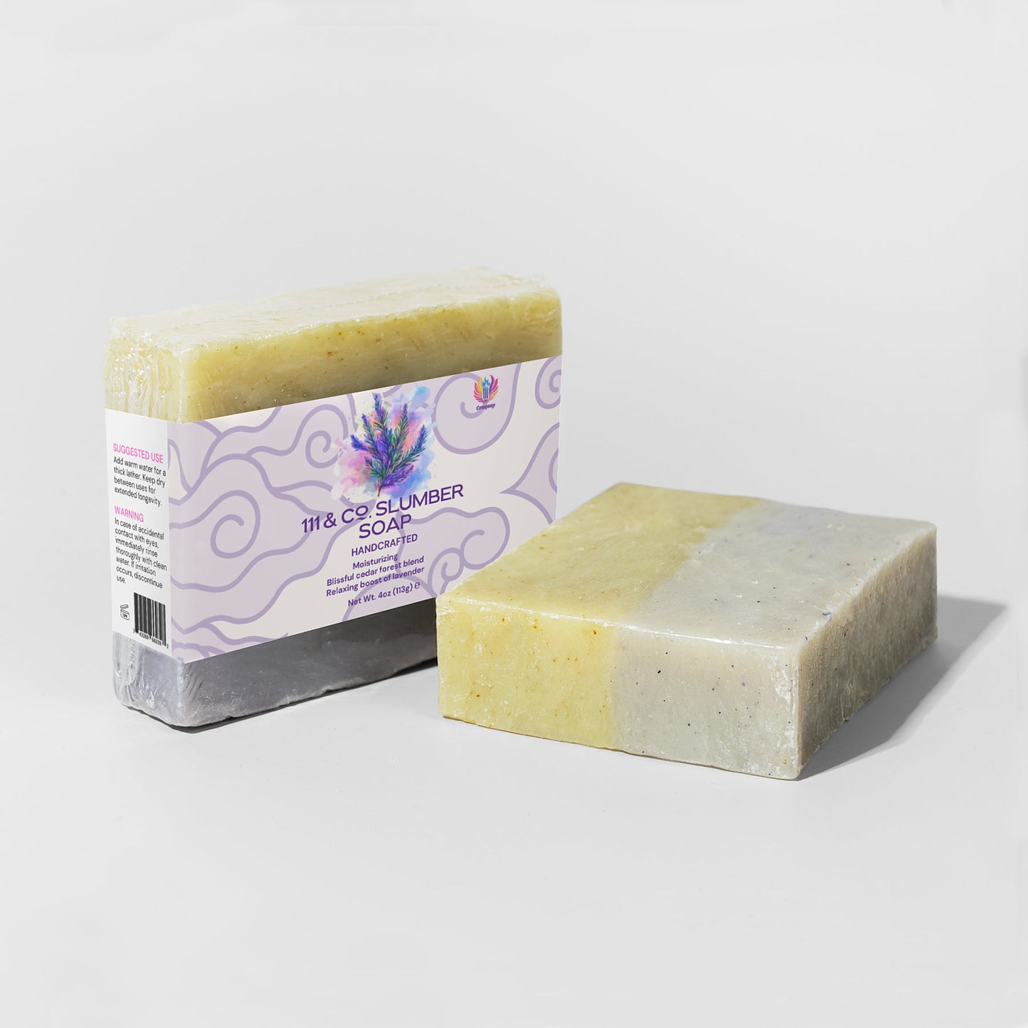 Two handcrafted soap bars are shown, one wrapped in a label reading 111 & Company Slumber Soap by 111 & Company, with lavender and fir needle imagery. The unwrapped bar reveals a marbled yellow and gray-green texture. Both rest on light gray surfaces, casting gentle shadows.