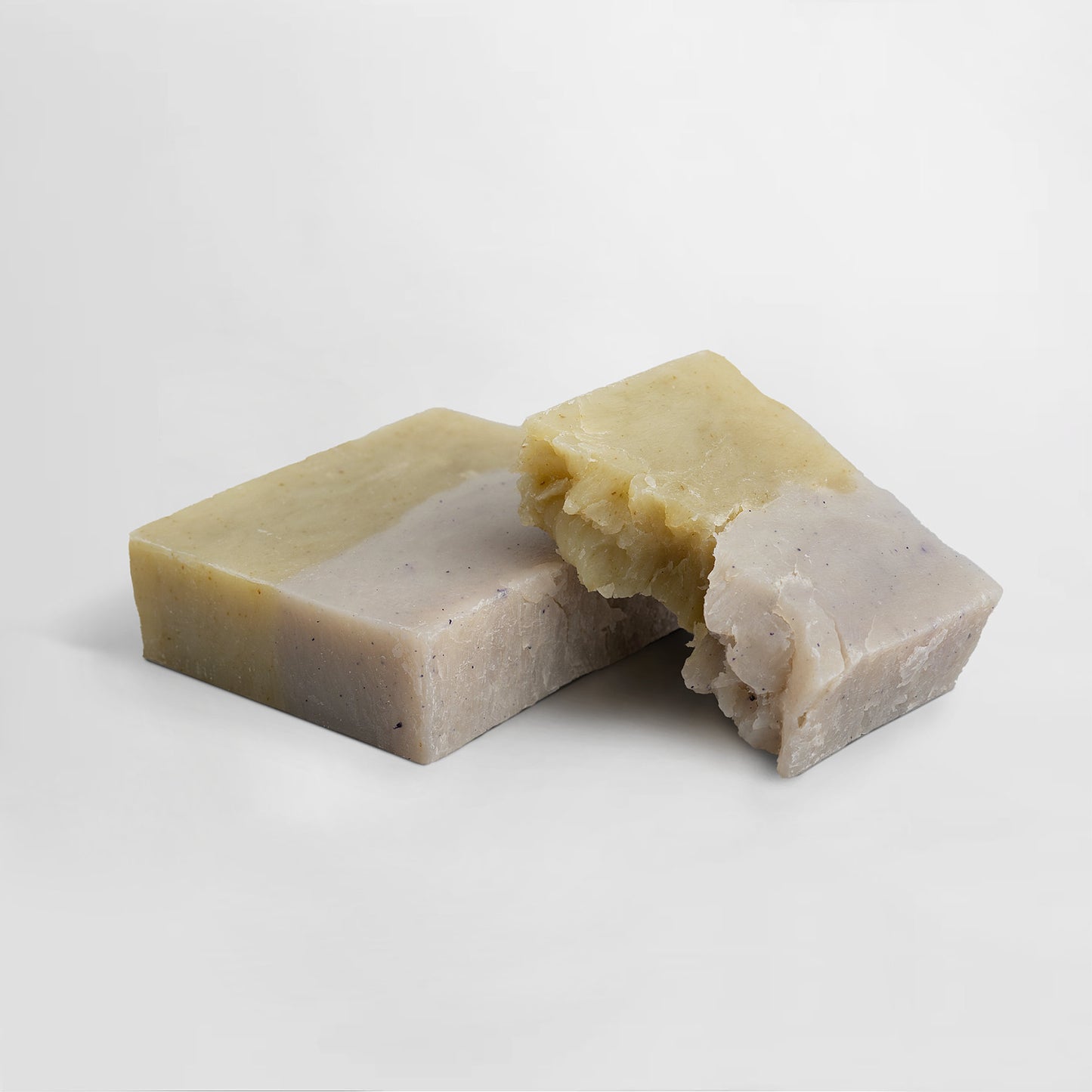 Two rectangular soap bars on a white background. One bar is intact with a smooth light green surface, while the other, an 111 & COMPANY SLUMBER SOAP by 111 & Company, is broken to reveal a textured interior with uneven edges. Both feature subtle speckled patterns and hint of fir needle scent.