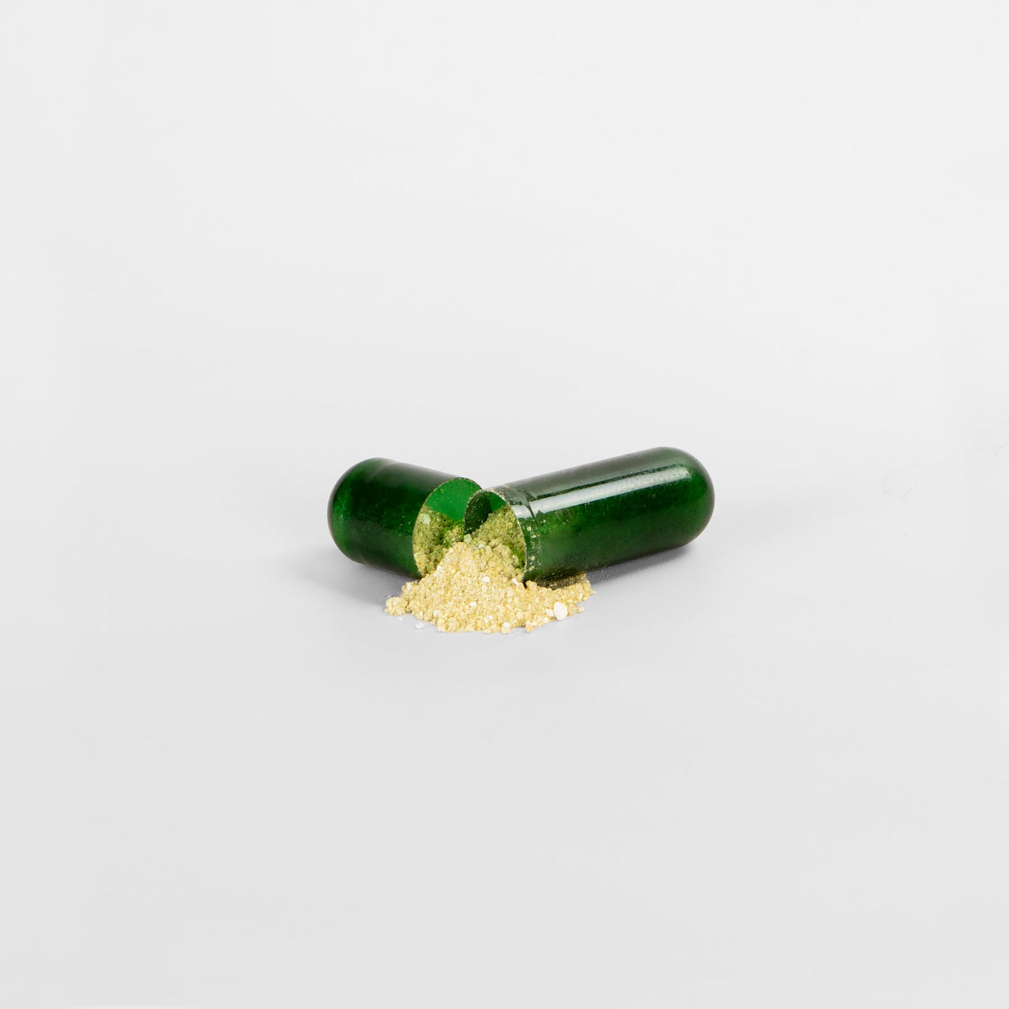 A dark green capsule, open on a white surface, spills fine beige powder forming a small pile. This product is 111 & COMPANY SUPER FAT BURNER WITH MCT by 111 & Company. The halves are aligned against a plain neutral background.