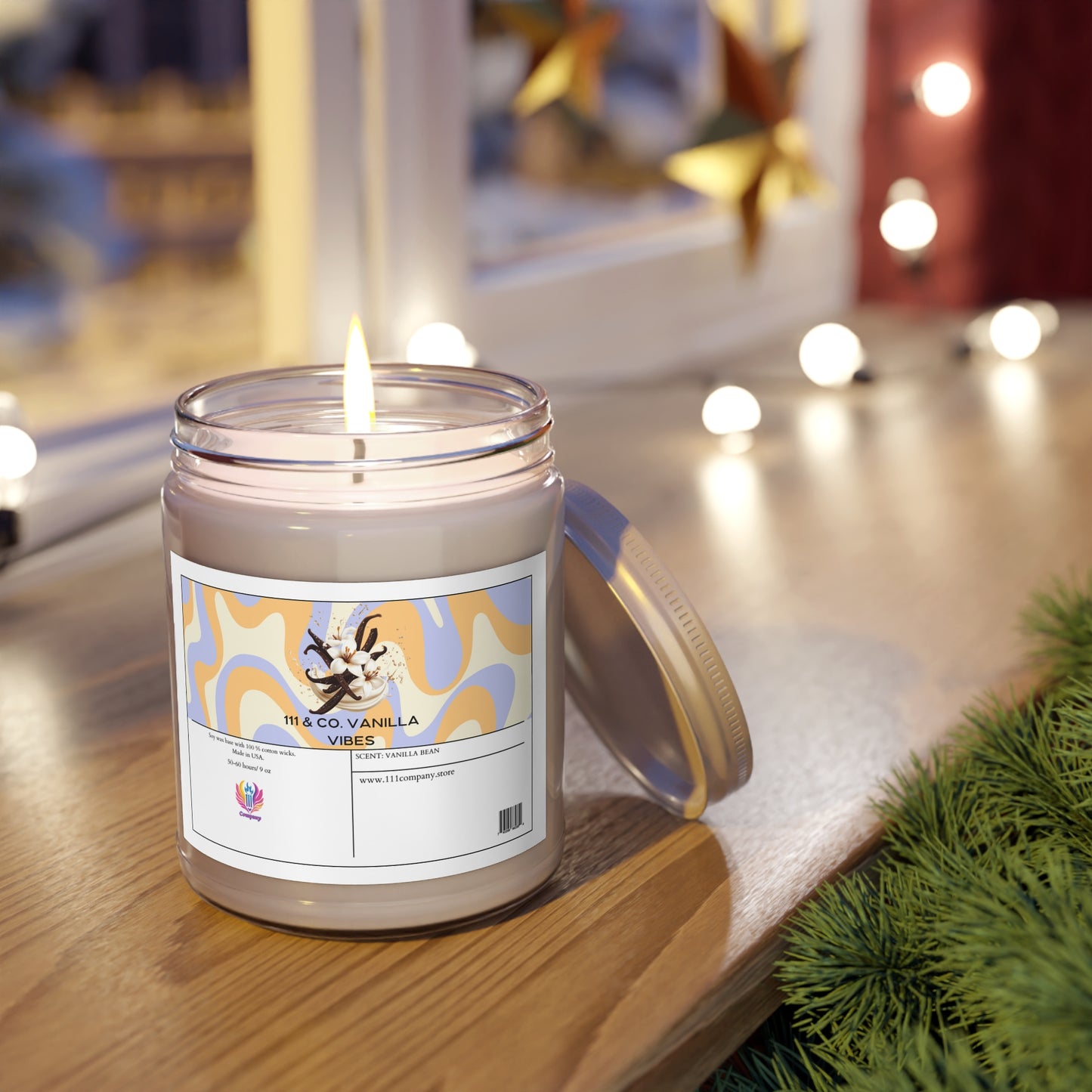 A lit 111 & Company Vanilla Vibes Vanilla Bean scented candle, crafted from a soy wax blend in a glass jar, sits on wood beside a window. The label depicts vanilla flowers and patterns; the lid rests next to it. String lights and green foliage enhance the cozy festive atmosphere.
