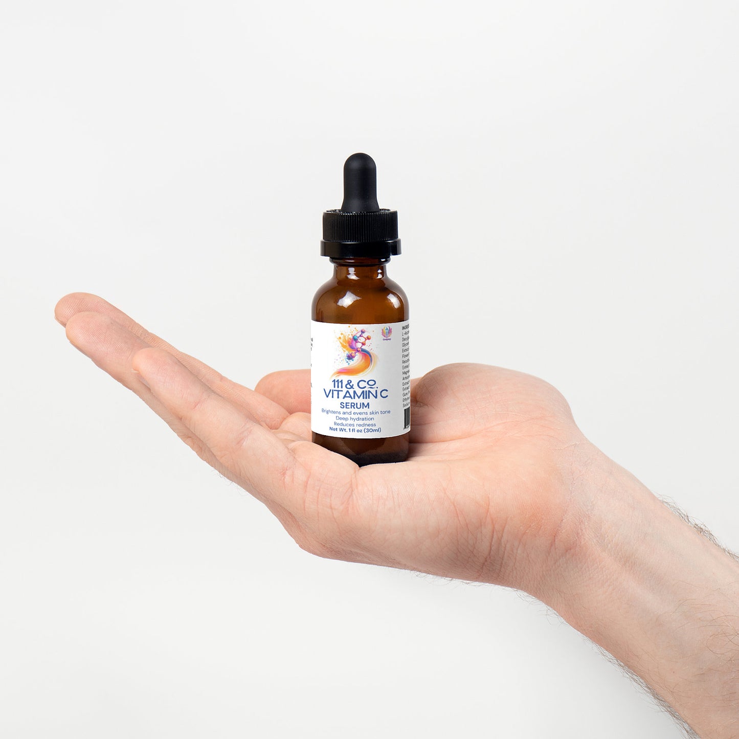 A hand is holding a small amber dropper bottle with a black cap against a plain white background. The label features colorful graphics and reads 111 & COMPANY VITAMIN C SERUM, by 111 & Company, highlighting its collagen-boosting properties. The palm faces upward.