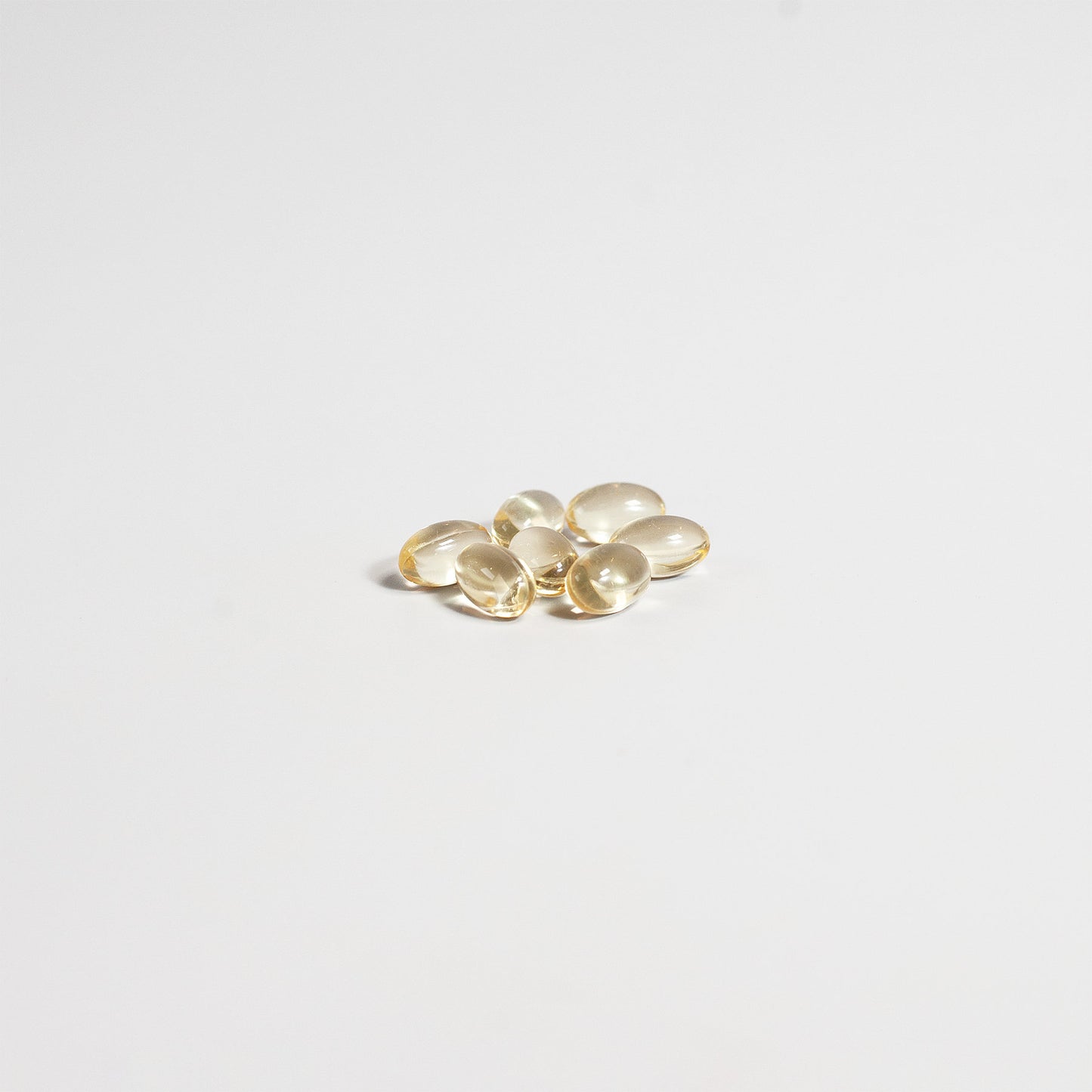 A small pile of oval, golden capsules rests on a plain white background, casting faint shadows. The glossy capsules reflect light, suggesting they could be soft gel Vitamin D3 supplements from 111 & Company designed to support bone health with 2,000 IU.