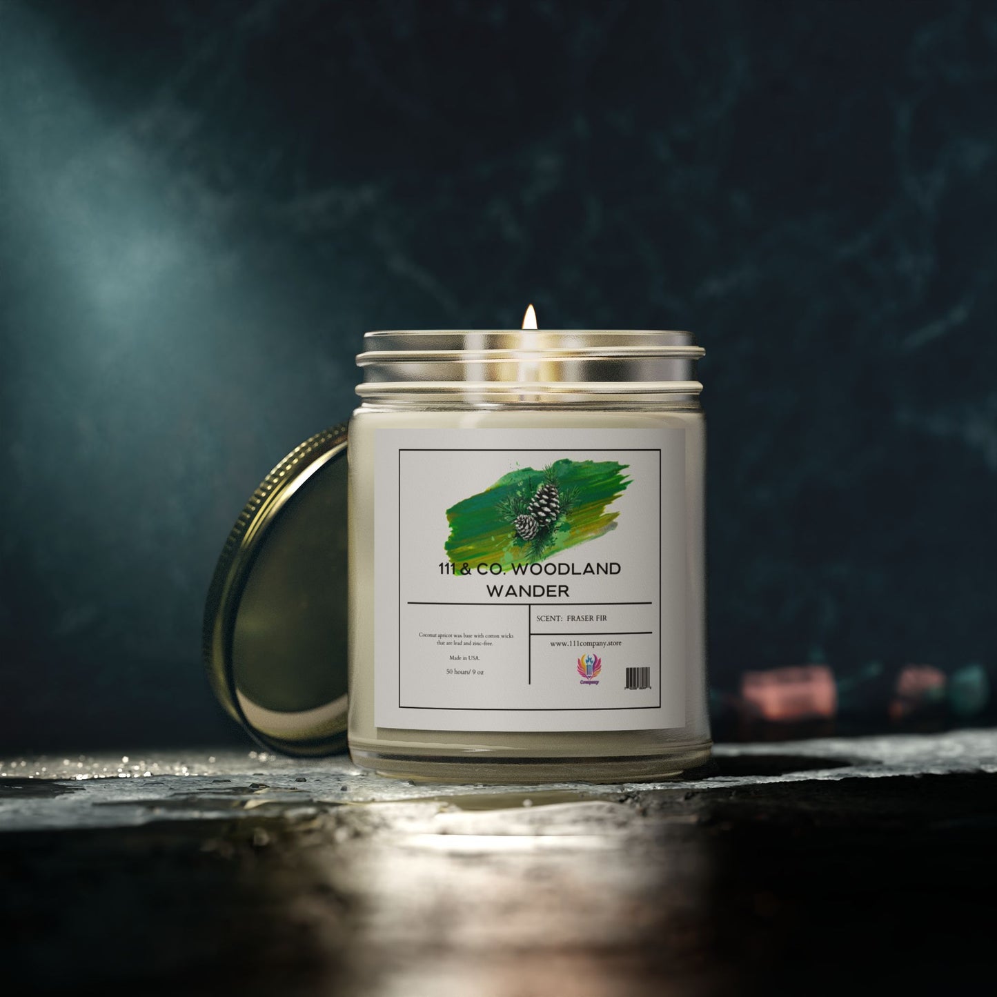 A 111 & Company Woodland Wander Fraser Fir candle by 111 & Company, in a 9oz clear jar with coconut apricot wax, sits on a dark surface. Its green and black abstract label contrasts the blurred colorful background, with its metal lid resting behind.