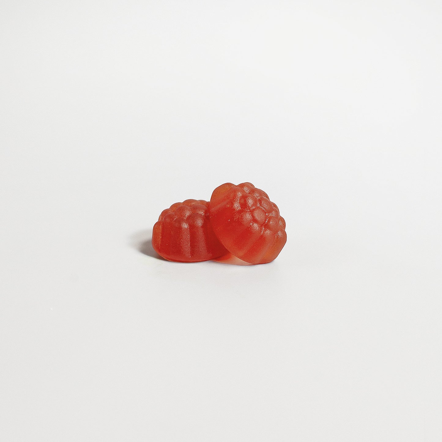 Two red 111 & COMPANY SLEEP WELL GUMMIES (ADULT) by 111 & Company, shaped like raspberries with a glossy finish and textured bumps, sit on a smooth white surface. The bright background accentuates these melatonin sleep supplements.
