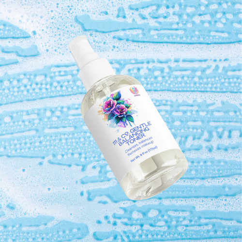 A clear spray bottle of 111 & COMPANY GENTLE BALANCING TONER for sensitive skin, adorned with a colorful flower design, rests on a blue background with white foam, conveying freshness and cleanliness. Brand: 111 & Company.