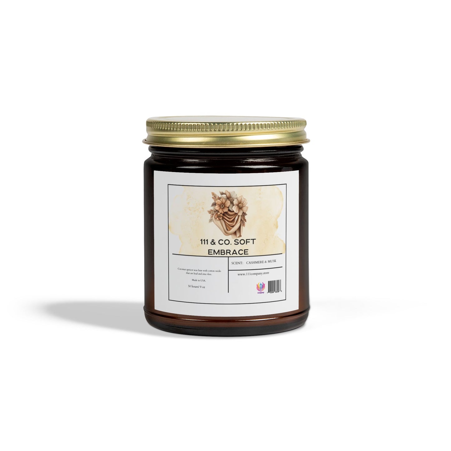 The Printify product, 111 & Co. Soft Embrace, is a Cashmere & Musk scented candle in an amber jar with a gold lid, adorned with a pine cone illustration. Made from eco-friendly coconut apricot wax, its hand poured in small batches. The reusable vessel casts a shadow on a white background.