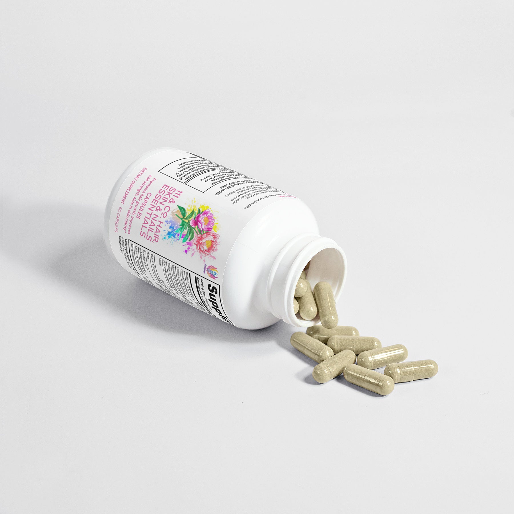 Gray capsules spill from a white bottle on its side, featuring the 111 & COMPNAY NOURISH HAIR, SKIN & NAILS CAPSULES label by 111 & COMPANY. The floral design hints at its benefits, enhancing your routine with purity against a plain white background.