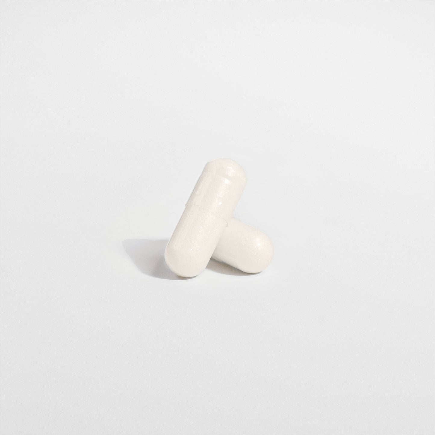 Two white capsules of 111 & Co. 5-HTP by 111 & Company form a cross on a plain white background, casting soft shadows for a clean, minimalist look, promoting serotonin support and enhancing emotional well-being.