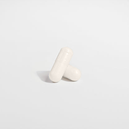 Two white capsules of 111 & Co. 5-HTP by 111 & Company form a cross on a plain white background, casting soft shadows for a clean, minimalist look, promoting serotonin support and enhancing emotional well-being.