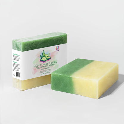 Two bars of 111 & Company Aloe & Cool Cucumber Soap rest on a white backdrop—one wrapped, the other showing its green and yellow layers. The label features cucumber slices and aloe vera, noted for soothing sensitive skin and hydrating effects.