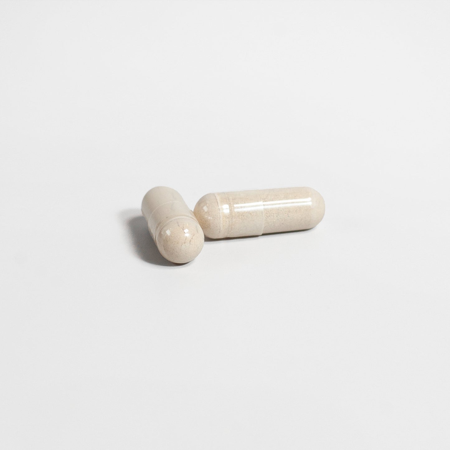 Two beige capsules of 111 & Company ALPHA ENERGY rest on a plain white surface, one horizontal and the other diagonally propped, embodying simplicity while supporting mens health and promoting cardiovascular wellness.