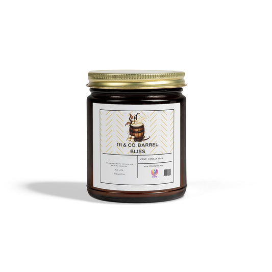 A dark amber glass jar with a gold lid features 111 & Co. Barrel Bliss in black text and a barrel illustration, highlighting eco-friendly coconut apricot wax and vanilla beans with Scent: Vanilla Bean and 9oz. The reusable vessel is set against a plain white background and branded by 111 & Company.