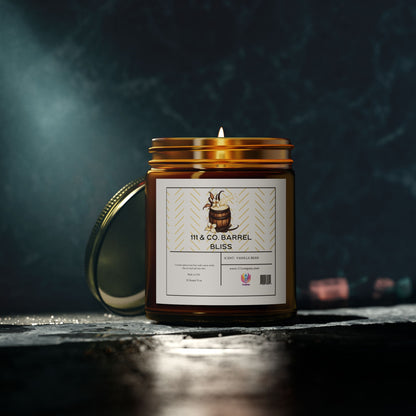 A lit 111 & COMPANY Barrel Bliss candle by 111 & Company, in an amber glass jar, rests on a dark surface. The label features a wooden barrel illustration and reads White + Vanilla Bean. The coconut apricot wax candle has its lid behind it, enhanced by soft lighting against the dark background.