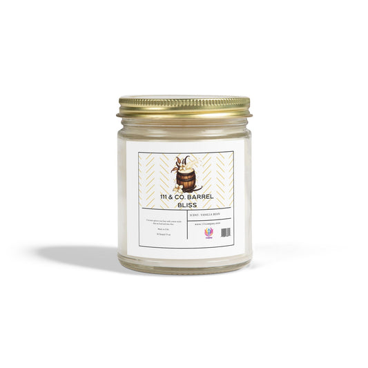 A clear jar candle by 111 & Company features a gold metal lid and a white label with a barrel design, reading 111 & Company Barrel Bliss and Scent: Vanilla Bean. Made from coconut apricot wax, the 9oz candle highlights its bourbon fragrance with barcode and logo below, casting a shadow on white.
